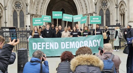 Liberty lawyers and staff outside the Royal Courts of Justice holding a banner that says "DEFEND DEMOCRACY"